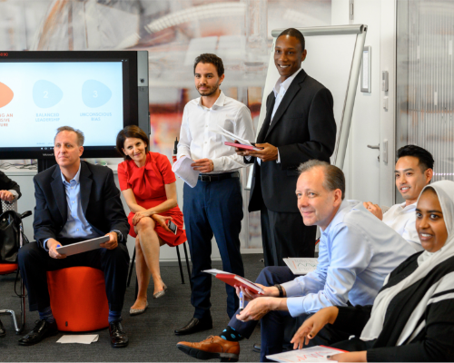 Et forskelligartet Henkel-team sidder sammen på et værksted og kigger ind på højttaleren 