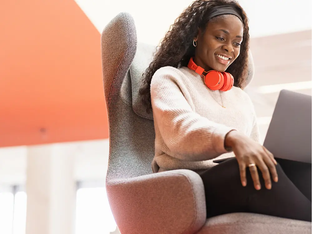 En Henkel-medarbejder sidder i en behagelig stol med sin bærbare computer på knæene. Hun smiler. 