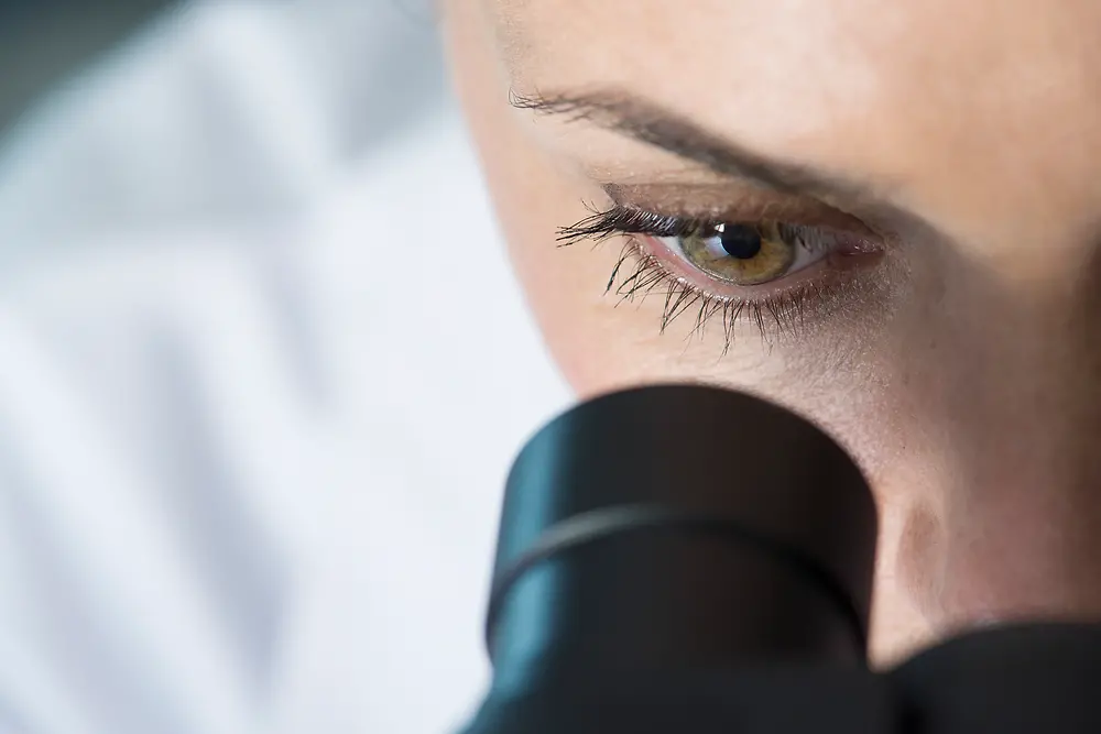 En kvindes øje kigger ind i et mikroskop
