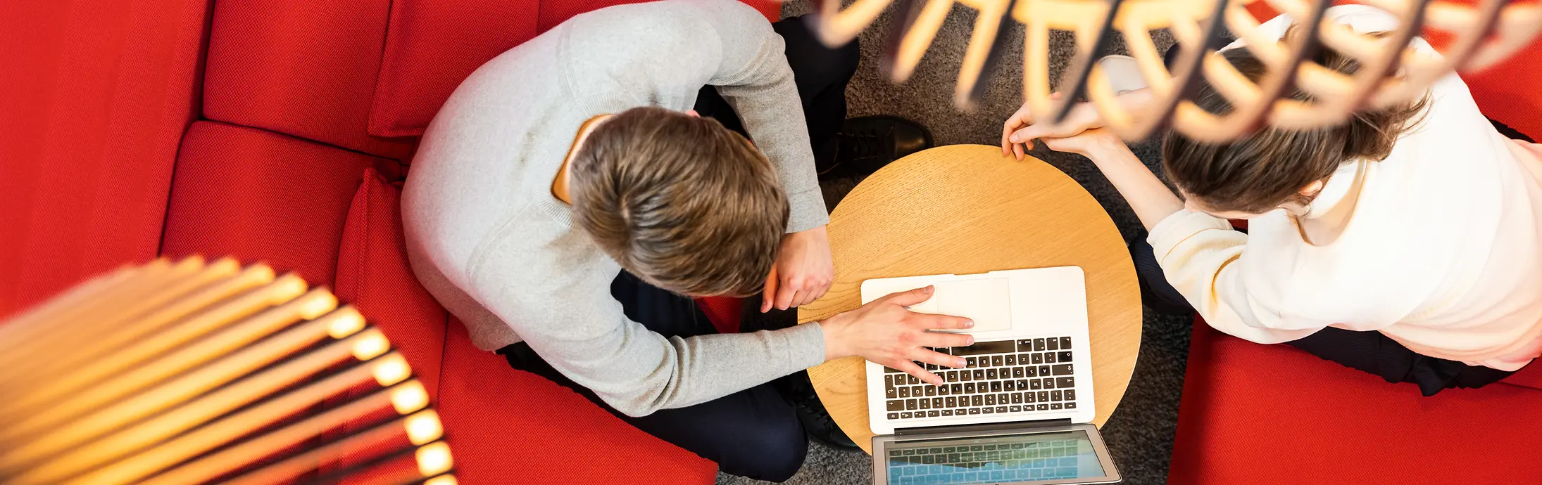 To personer sidder i en rød sofa og arbejder sammen på en computer.