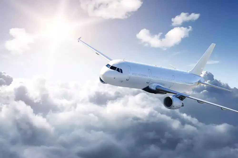 Et hvidt passagerfly, der flyver over bløde skyer på en klar himmel, med sollys, der skinner fra øverste venstre hjørne